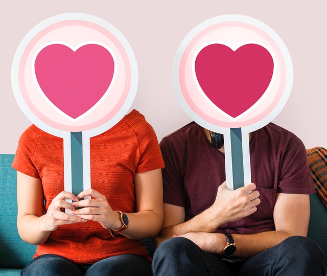 Muž a žena si pred tvárou držia ceduľky s veľkými ružovými srdcami.jpg