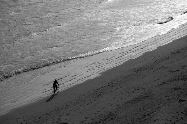 Osoba ide na bicykli po pláži počas prílivu.jpg
