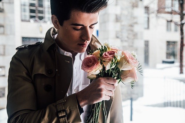 Mladý muž v hnedom kabáte drží v rukách kyticu kvetov.jpg